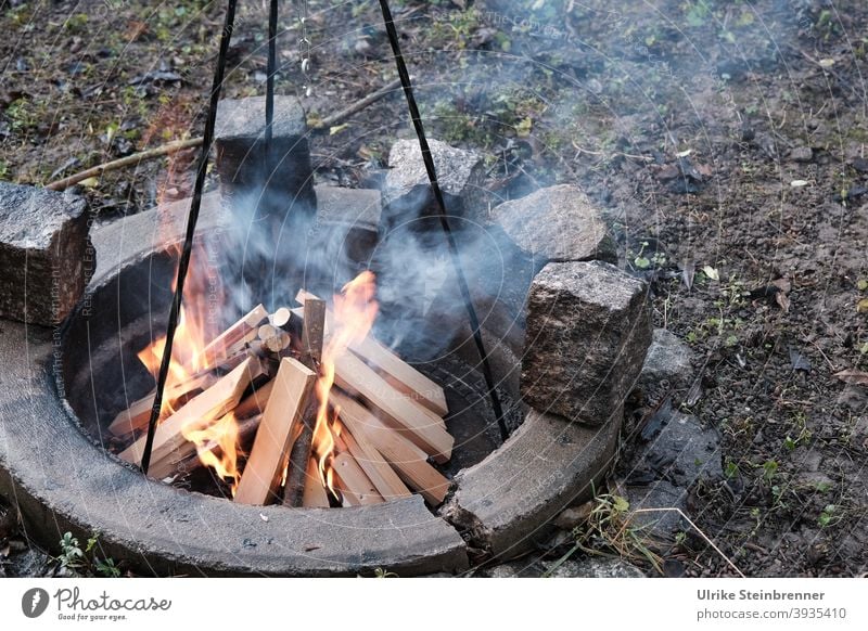 Anzünden eines Lagerfeuers zum Kochen Feuer Brennholz Holzscheite Kochfeuer Dreibein Feuer machen brennen Flammen anheizen entzünden heiß Feuerstelle Wärme