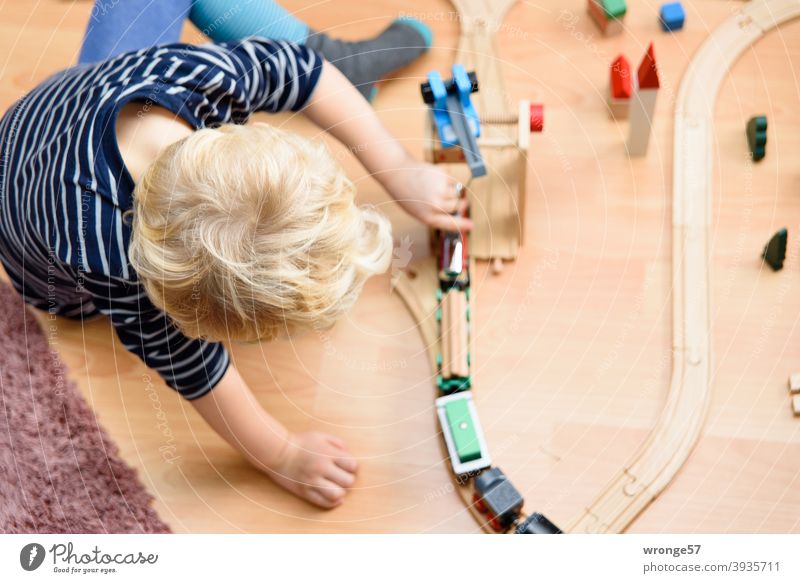 Kleiner blonder Jungen spielt mit einer Holzeisenbahn auf dem Fußboden kleiner Junge 4 Jahre alt 4 jährig spielen Spiel Eisenbahn Kind Kindheit Spielen