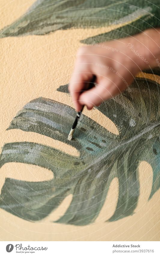 Männlicher Künstler malt an der Wand zu Hause Farbe Anstreicher Blatt Mann Innenbereich Appartement dekorieren Fensterblätter männlich grün kreativ Stil