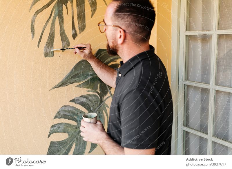 Männlicher Künstler malt an der Wand zu Hause Farbe Anstreicher Blatt Mann Innenbereich Appartement dekorieren Fensterblätter männlich grün kreativ Stil