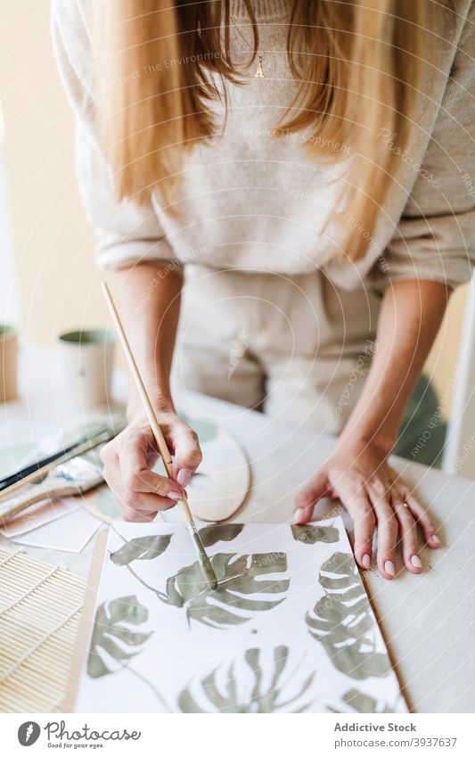 Crop Painter erstellt Bild von Monstera Blätter auf Papier Künstler Farbe Anstreicher Frau Fensterblätter Blatt Pflanze Werkstatt Pinselblume Tisch Malerei grün