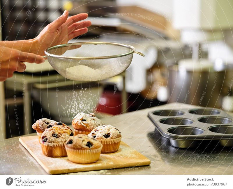 Chefkoch bestreut Muffins mit Puderzucker Gebäck Konditorei bestäuben Pulver Sieb Küchenchef gebacken vorbereiten professionell Zucker Teigwaren kulinarisch