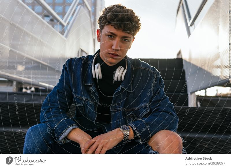 Junger Mann mit Kopfhörer auf der Treppe sitzend zuhören Großstadt Drahtlos jung männlich sich[Akk] entspannen krause Haare Audio Freude Optimist positiv ruhen