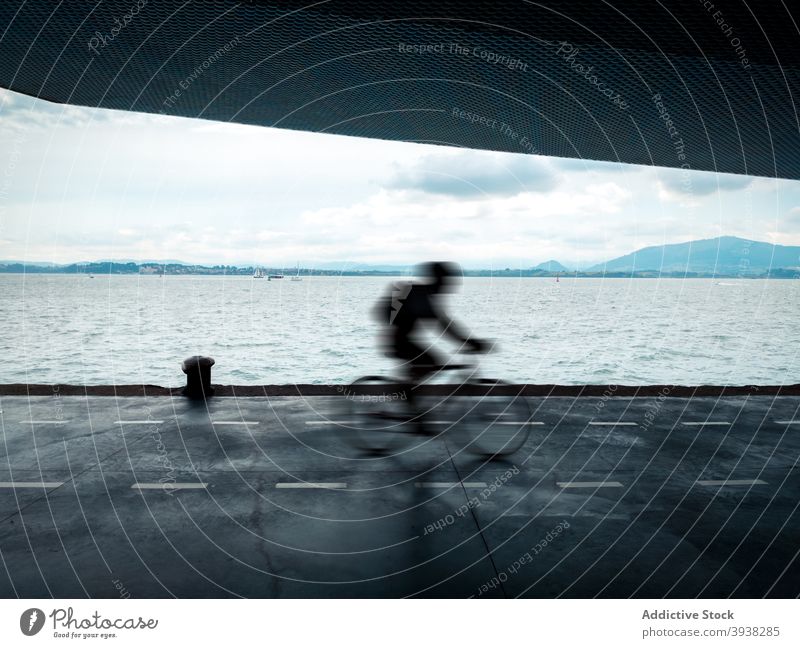 Unerkennbarer Mann auf dem Fahrrad entlang der Uferpromenade an einem bewölkten Tag Mitfahrgelegenheit Straße MEER Natur Stauanlage Aktivität Geschwindigkeit