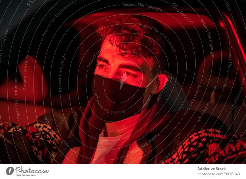 Anonymer Mann fährt beleuchtetes Auto in medizinischer Maske während der Pandemie Laufwerk PKW Nacht Konzentration Coronavirus neue Normale neonfarbig Großstadt
