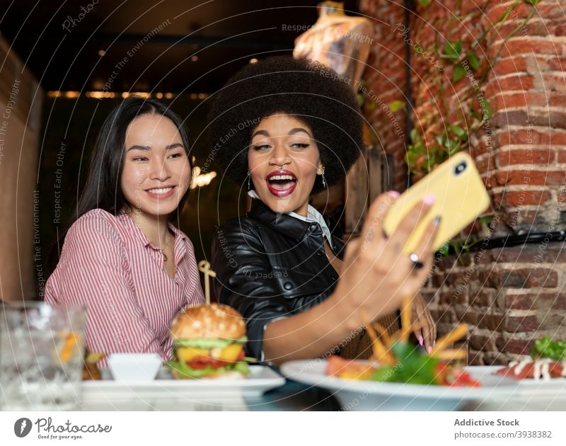 Multirassische Freundinnen nehmen Selfie beim Abendessen im Restaurant Smartphone Zusammensein heiter Telefon lustig Grimasse Lebensmittel jung Frauen