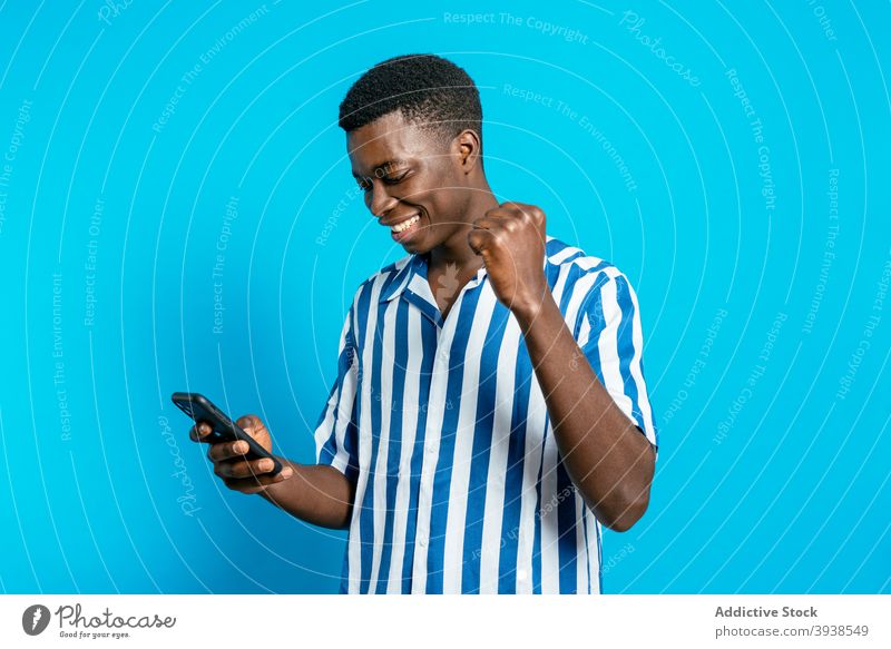 Schwarzer Mann feiert den Sieg mit geballter Faust Gute Neuigkeiten heiter feiern Gewinner die Faust ballen Glück Freude Smartphone männlich schwarz ethnisch
