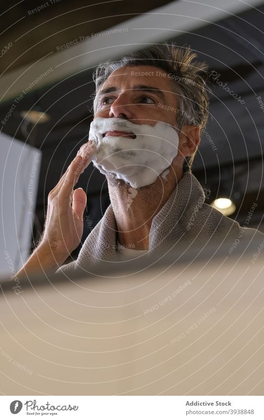 Gut aussehender Mann, der Rasiercreme aufträgt anwendend Lebensmitte Reflexion & Spiegelung Bad zu Hause Rasur Hautpflege Vorderansicht Porträt männlich