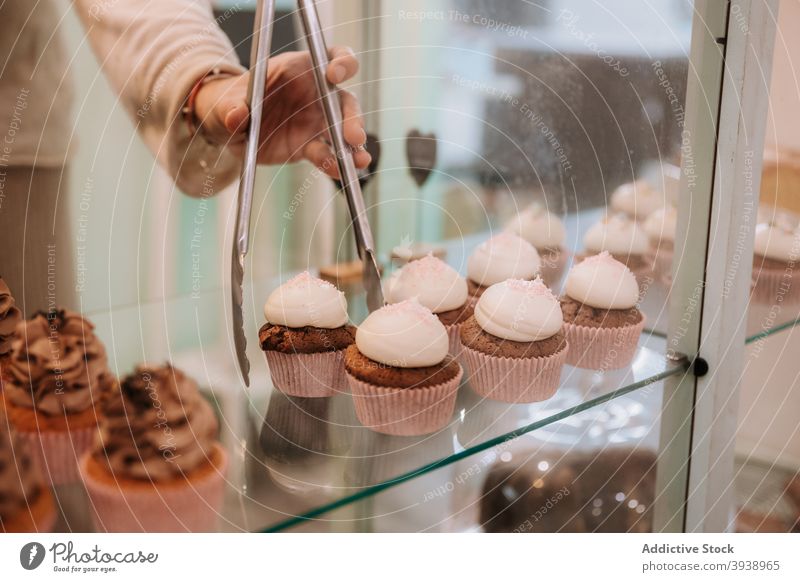 Verkäuferin nimmt Cupcake aus der Auslage im Süßwarengeschäft Konditorei süß nehmen Anzeige Bonbon Werkstatt Dessert Sahne tong Frau Einzelhandel Wahl Laden