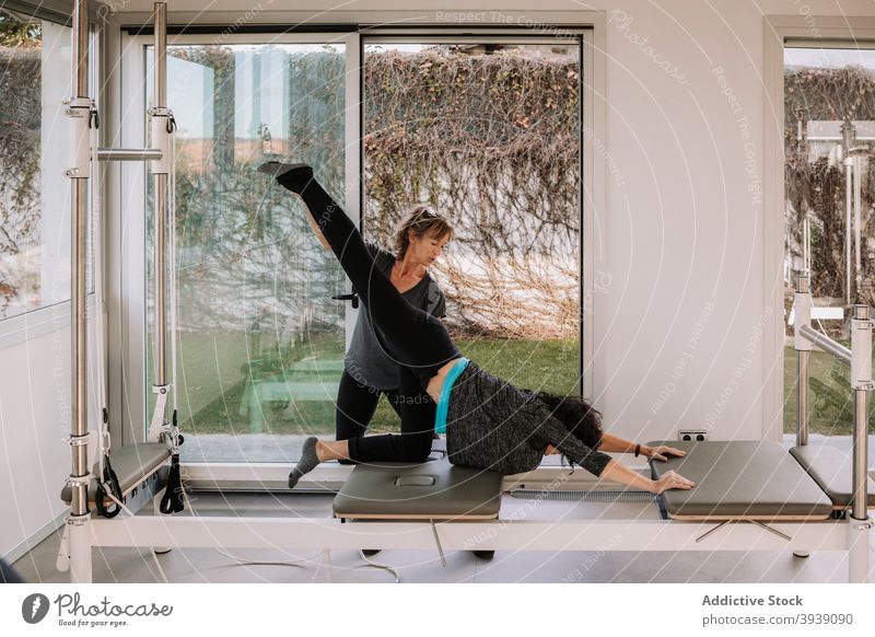 Frau macht Yoga mit Hilfe von Trainer Pilates Frauen Reformer Ausbilderin nach unten gerichtete Hundehaltung Asana Pose Gerät Hilfsbereitschaft Fitnessstudio