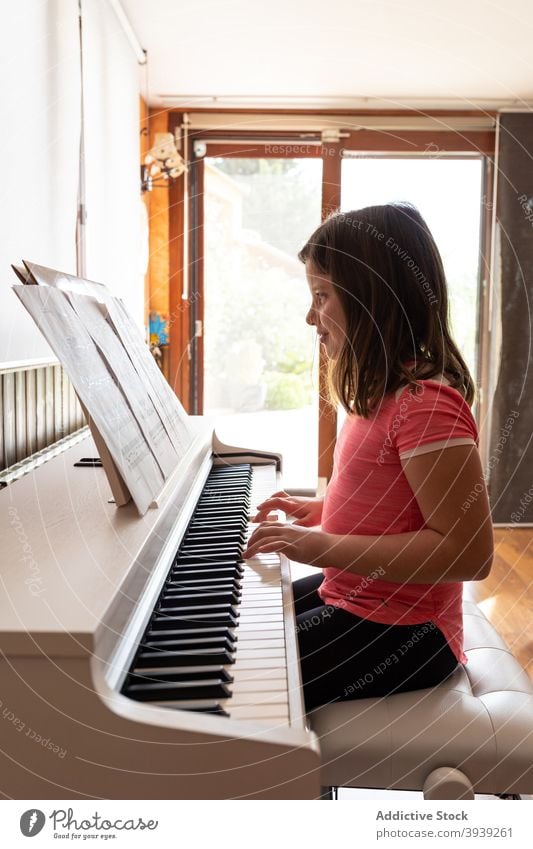 Lächelndes Kind spielt Klavier in gemütlichen Zimmer im Tageslicht spielen Probe lesen Musik Hinweis Musiker heimwärts Instrument positiv Melodie Mädchen lässig