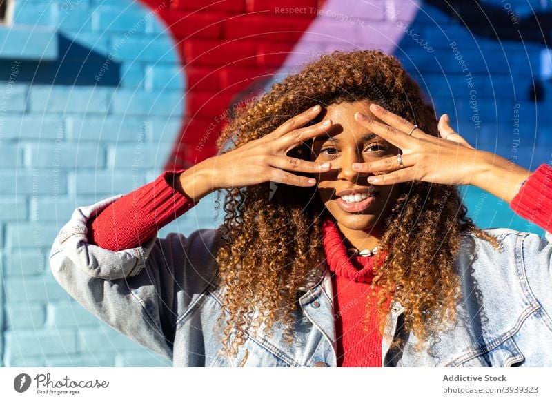 Fröhliche junge schwarz gestikulieren und lächelnd in der Nähe Wand mit Graffiti Frau Gesicht berühren Lächeln Glück Straße Subkultur Stil positiv Straßenkunst