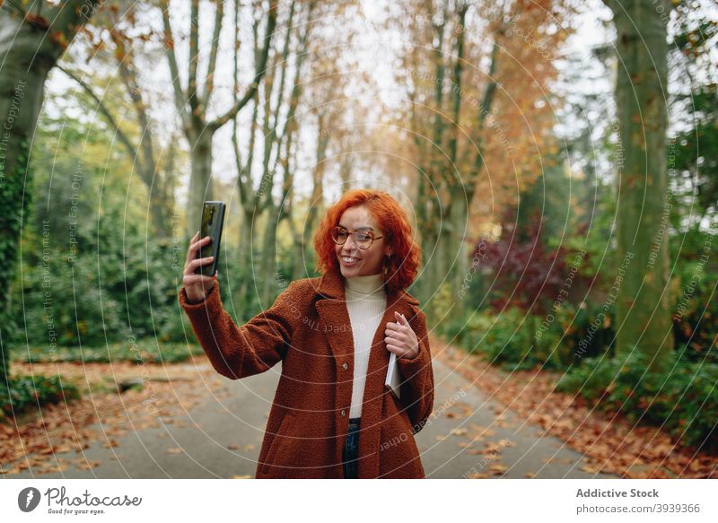 Positive Frau benutzt Mobiltelefon im Park sprechen Smartphone Rotschopf rote Haare heiter genießen Gespräch diskutieren Gasse Mantel Herbst Apparatur Glück