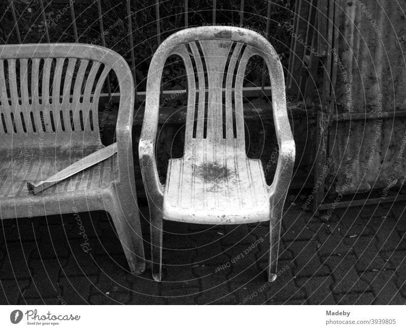 Verschmutze alte Gartenmöbel aus weißem Kunststoff beim Sperrmüll auf dem Gehweg Stuhl Bank Camping Campingmöbel Sitzen Sitzgarnitur Schwarzweiß Verlassen