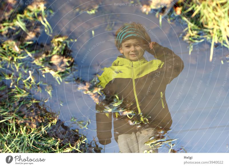 surreal II - Porträt eines Jungen in schwarz-gelber Jacke und grauer Hose spiegelt sich in einer Pfütze auf einem Feldweg Mensch Kind Spiegelung Gras Winter