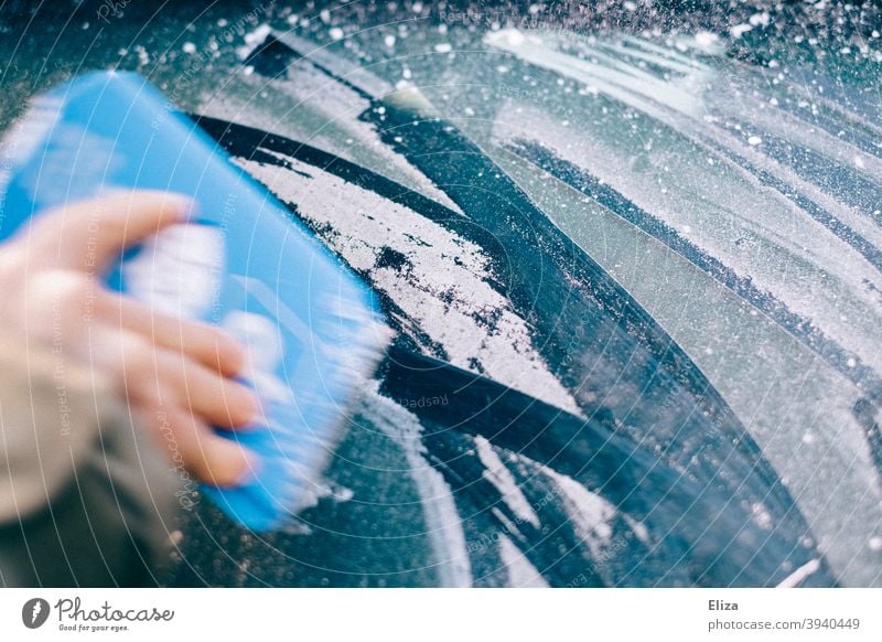 Hand kratzt im Winter mit einem Eiskratzer die vereiste Autoscheibe frei Frost kratzen Scheibe gefroren PKW Autofenster Windschutzscheibe blau kalt