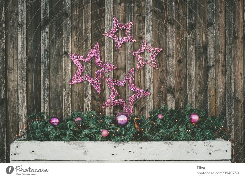 Weihnachtsdekoration aus lila Sternen und Christbaumkugeln an einer Holzwand Weihnachten & Advent Weihnachtsschmuck Tannenzweige Schuppen außen festlich