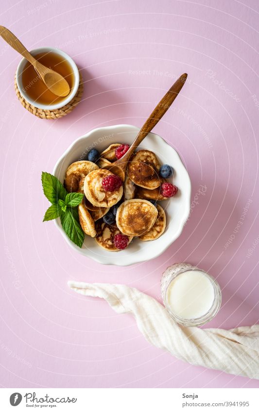 Frühstück mit Mini Pancakes und frischen Beeren in einer Schüssel auf einem rosa Hintergrund. Miniatur lecker Milch Honig Draufsicht süß Lebensmittel Ernährung
