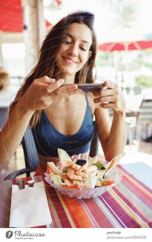 Junge Frau, die ihren Salat mit einem Smartphone fotografiert, während sie in einem Restaurant sitzt Lebensmittel Salatbeilage Gesundheit Telefon Mobile