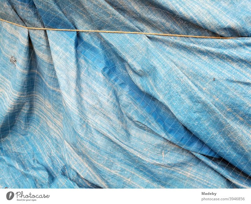 Verwaschene blaue Plane aus Kunststoff gut verschnürt als Schutz vor Regen und Sturm Ebene Schutzplane Jeansstoff Sickerwasser Regenschutz Plastik hintergrund