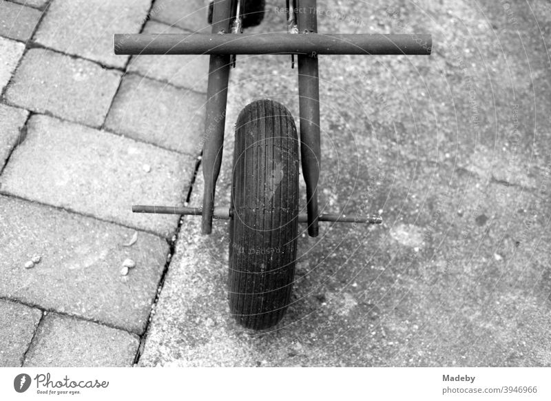 Vorderrad eines selbstgebaute Dreirad aus Teilen einer alten Schubkarre auf grauen Pflastersteinen und grauem Beton in klassischem Schwarzweiß Eigenbau