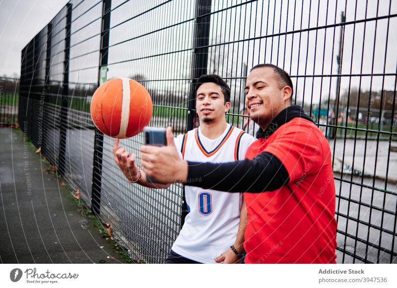 Freunde machen ein Selfie am Zaun eines Basketballplatzes im Freien. Spieler Gericht horizontal Teenager Vitalität Aspirationen Basketballer männlich