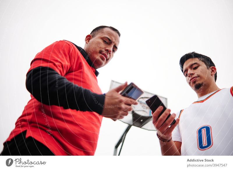 Tiefwinkelaufnahme von zwei Freunden, die ihr Telefon auf einem Basketballplatz überprüfen. Spieler Gericht horizontal Teenager Vitalität Aspirationen