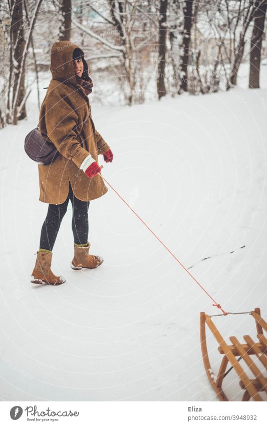 Eine Frau zieht einen Schlitten durch den Schnee im Winter Rodeln Freude lachen winterlich brünett Schneelandschaft verschneit Mantel weiß Natur kalt Mensch