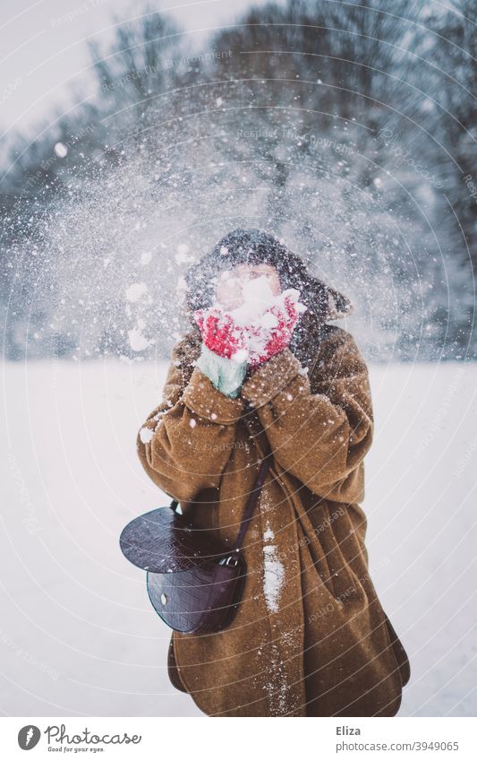 Eine Frau mit einer Schneewolke vor dem Gesicht pusten winterlich Winter jung draußen schneien Schneegestöber Schneelandschaft Natur Winterstimmung Wintertag