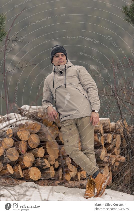 Junger Mann im Feld auf Brennholz im Winter mit Schnee Hintergrund schön Stiefel Nahaufnahme Kleidung kalt Konzept Design Mode Fuß Schuhe Wald Frost wandern Eis