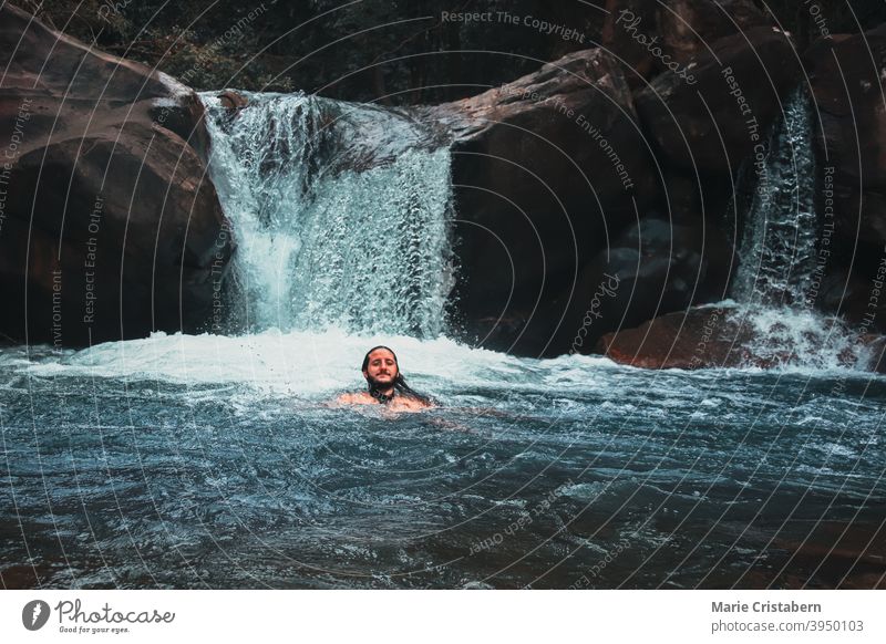 Ein Mann, der ein Bad im Wasserfall genießt Schwimmen in einem Wasserfall zurück zur Natur Outdoor-Veranstaltung Schwimmsport Nur ein Mann aktiver Lebensstil