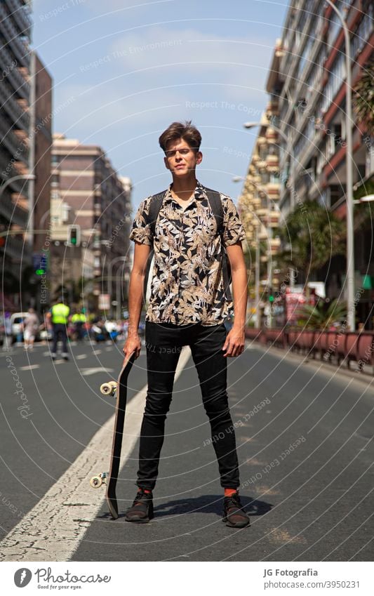 Porträt von authentischen jungen Mann mit Skateboard in der Mitte der Straße. Typ Skateboarderin urban Model retro Einstellung Aussehen Starrer Blick Gesicht