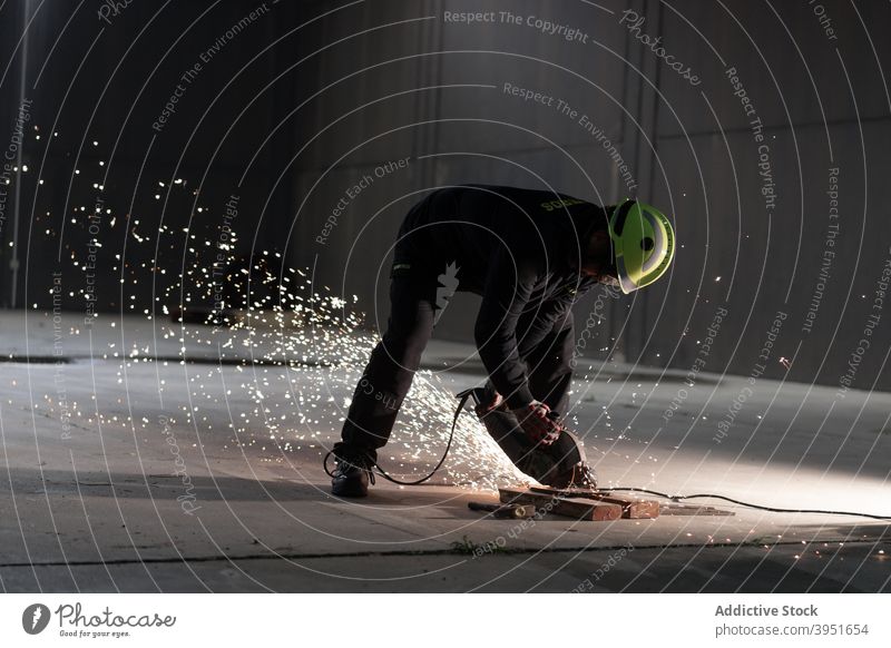 Anonymer männlicher Techniker schneidet Metall mit Kappsäge auf der Straße bei Nacht Mann Schweißer Säge bügeln Funken Metallbearbeitung Herstellung Werkzeug