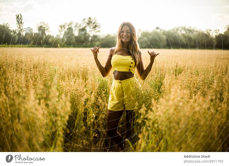 Frau zeigt Shaka-Geste im Feld gestikulieren heiter Zeichen Symbol Sommer Park Natur salburua Vitoria Gasteiz Spanien gelb Outfit Optimist positiv froh genießen