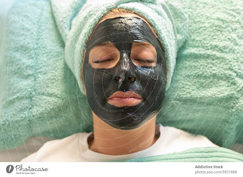 Junge Frau mit schwarzer Gesichtsmaske, die im Salon Gesichtsbehandlung Hautpflege Ton Mundschutz Verfahren Kosmetik Erstaunen wow gestikulieren Freude