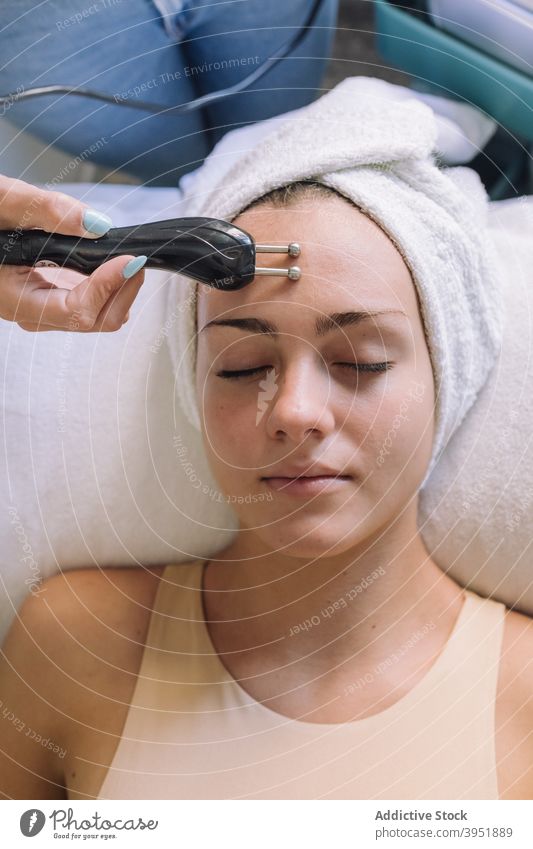 Entspannte junge Frau auf der Liege liegend mit geschlossenen Augen während einer Mikrostrom-Gesichtsbehandlung Frauen Hautpflege verjüngen Anti-Aging Verfahren