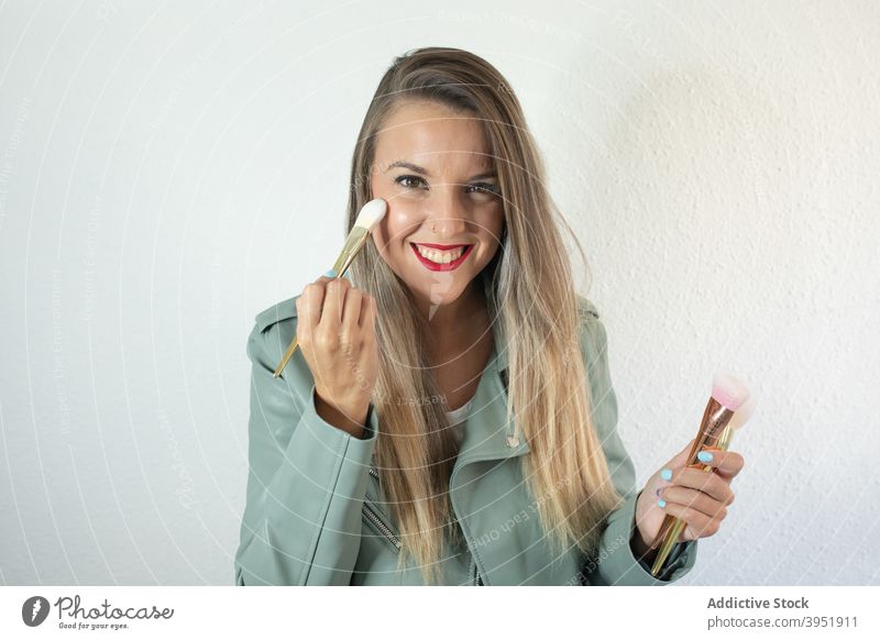 Lächelnde junge Visagistin beim Auftragen von Make-up mit Pinseln Frau Bürste bewerben Fundament Gesicht Pulver Stil Porträt selbstbewusst trendy Freude