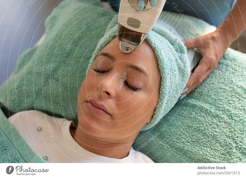 Crop Kosmetikerin tun Laser Haarentfernung Verfahren für junge Frau in Schönheit Studio Frauen Epilation Behaarung entfernen Klient Lügen Augen geschlossen