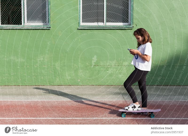 Stylish Mädchen mit Smartphone während Skateboarding auf Sportplatz benutzend Kreuzfahrtschiff-Brett Sportpark Süchtige Aktivität Hobby soziale Netzwerke Stil