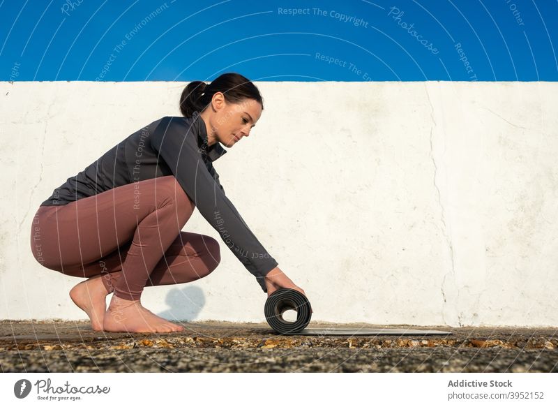 Schlanke Frau mit Yogamatte am sonnigen Tag Unterlage vorbereiten üben schlank Windstille Harmonie Sportbekleidung Zen ruhig Barfuß schlanke Wellness Gesundheit