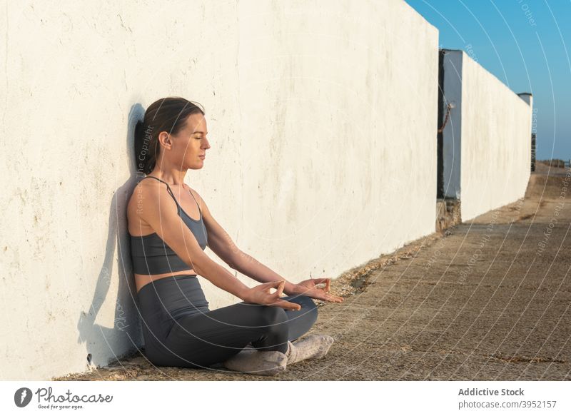 Schlanke Frau meditiert in der Nähe der Wand Yoga meditieren Lotus-Pose Asana padmasana Barfuß Zen Harmonie Mudra gestikulieren Wellness friedlich Gleichgewicht