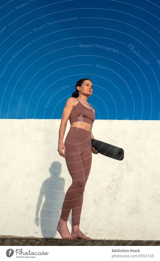 Ruhige Frau mit Yogamatte stehend in der Nähe der Wand Unterlage schlank ruhig Sportkleidung bereit vorbereiten Sportbekleidung Harmonie Beton Himmel blau