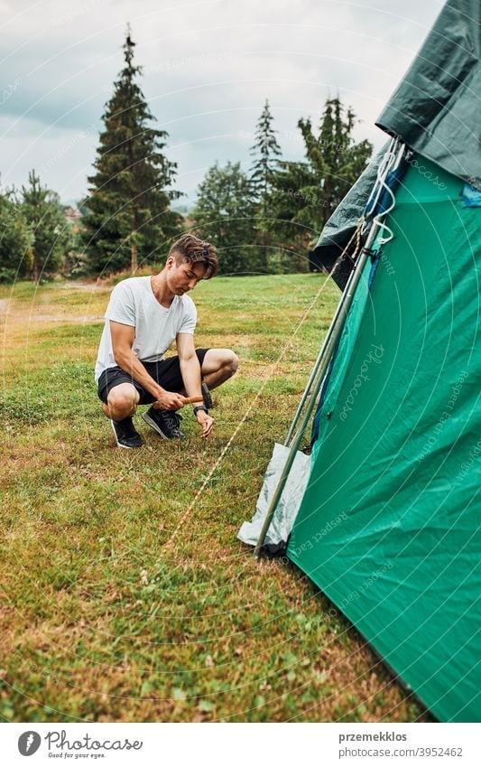 Junger Mann beim Aufbau eines Zeltes auf dem Campingplatz während der Sommerferien Reise Pfahl Zapfen Hammer Gras nach oben Einstellung Setzen Pitsching