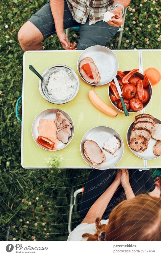 Familie beim Frühstück im Freien auf dem Campingplatz in den Sommerferien authentisch wirklich Banane gekochtes Fleisch langsames Leben Tischdecken im Freien