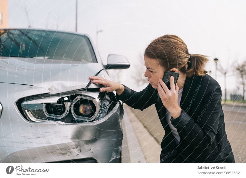 Ernste junge Dame spricht am Telefon und überprüft Auto Schäden nach Unfall Frau Telefonanruf prüfen Schaden PKW Absturz gebrochen verärgert Smartphone reden