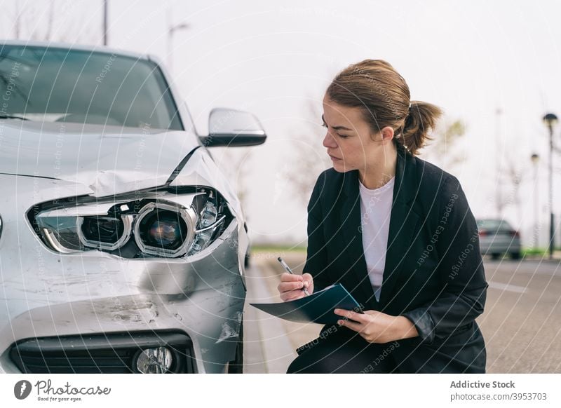 Junge weibliche Versicherungsagentin schreibt Bericht auf Klemmbrett nach Autounfall Frau schreiben Unfall Vermittler Konzentration PKW Absturz Arbeit jung