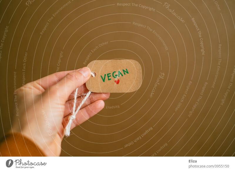 Hand hält ein Etikett auf dem das Wort vegan geschrieben steht. Vegane Lebensweise. vegane Lebensweise vegane Produkte kaufen Konsum Waren ohne Tierleid
