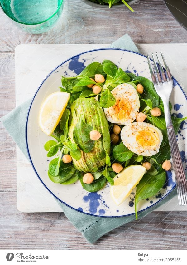 Avocado-Spinat-Salat mit Kichererbsen und Eiern Lebensmittel Gemüse Salatbeilage hart gekocht serviert Zitrone grün Blatt Gesundheit Speise Teller Tisch hölzern