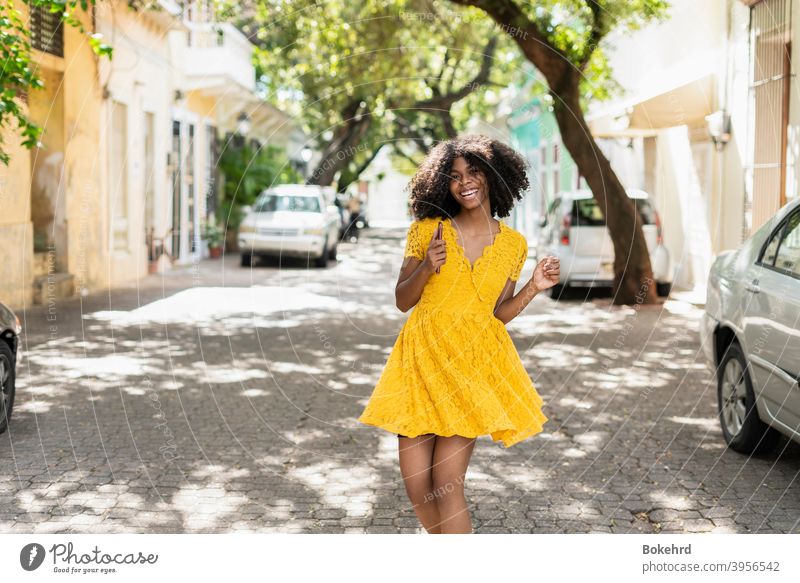Junge schwarze Frau mit lockigem Haar, in gelbem Kleid und mit Stilen, Haltung, lachend, glücklich Individualität Ethnizität Haut Lächeln Frisur Nachricht