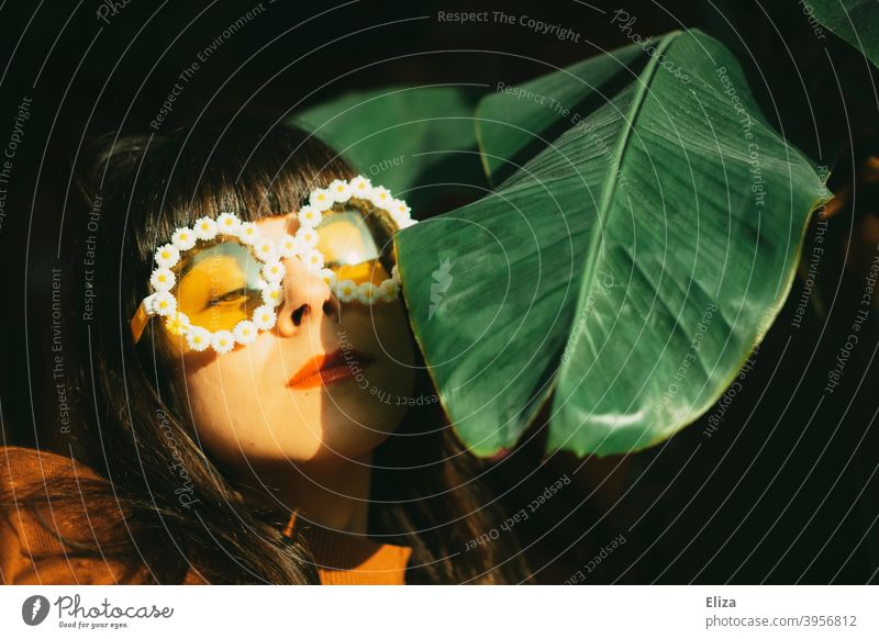 Frau mit lustiger Blümchen-Sonnenbrille genießt den Sonnenschein; das Bananenblatt auch. Hippie Brille Junge Frau Gesicht Portrait lachen authentisch